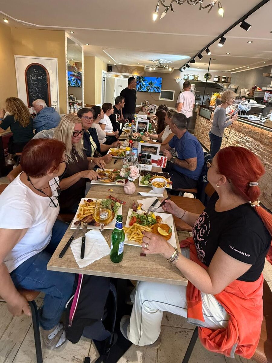 Friends around a long table inside, with the bar and the kitchen in the background